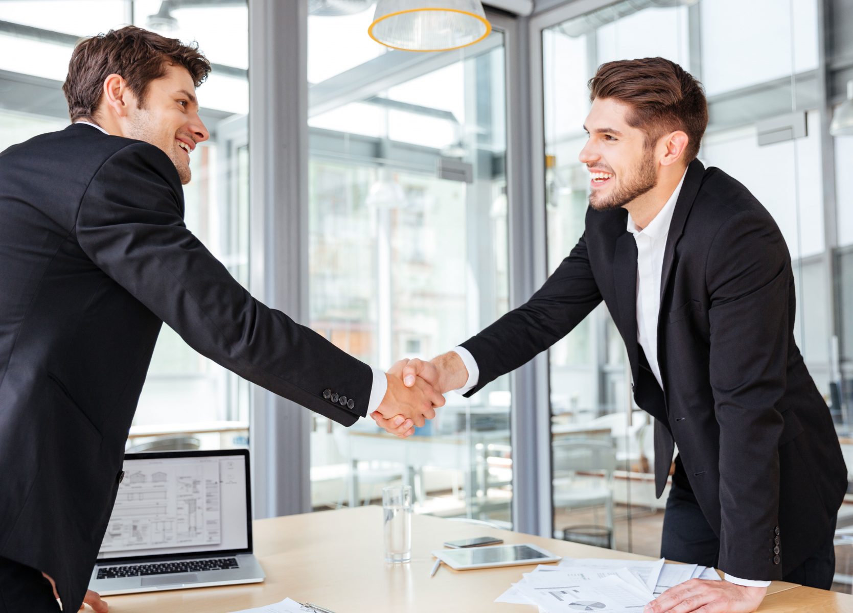 Two cheerful successful young businessmen shaking hands on business meeting